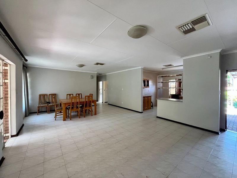 Spacious open-plan living and dining area featuring tiled flooring, neutral walls, and a functional kitchen layout with a breakfast counter.