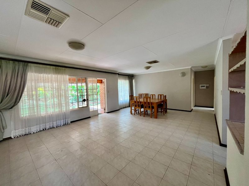 Spacious open-plan living and dining area featuring neutral tiled flooring, ducted air conditioning, and large windows providing natural light and access to the patio.