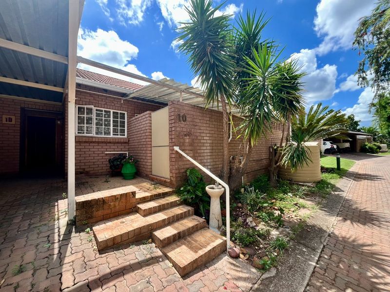 Front exterior view of a brick flat featuring a covered entrance, paved walkway, and established garden area with a water tank.