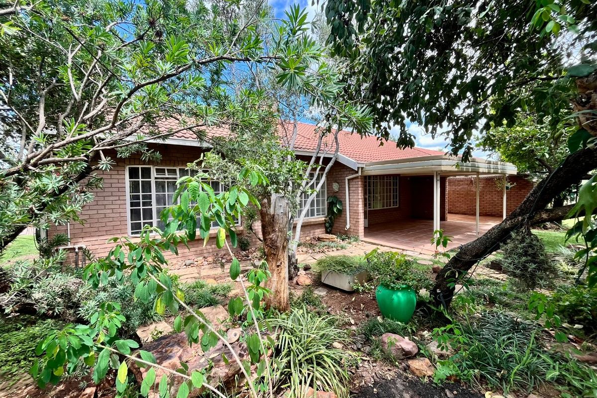 Rear view of the property featuring a brick facade, tiled roof, and a covered patio area surrounded by a mature garden.
