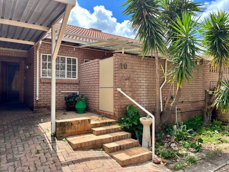 Front exterior view of a brick-faced flat featuring a paved driveway, covered carport, and entrance steps with a metal handrail.