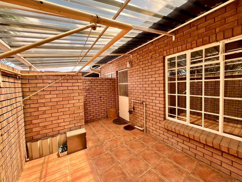 A covered outdoor patio area featuring brick walls, tiled flooring, and a corrugated plastic roof structure, providing a functional space for outdoor use.
