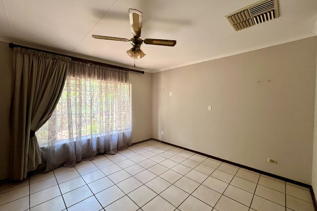 A spacious, empty bedroom featuring neutral tiled flooring, a ceiling fan, and an integrated air conditioning vent, ready for personalization.