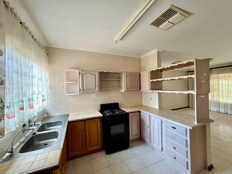 A dated kitchen featuring tiled countertops, built-in cabinetry, a double bowl sink, and a freestanding electric stove, offering potential for modernization.