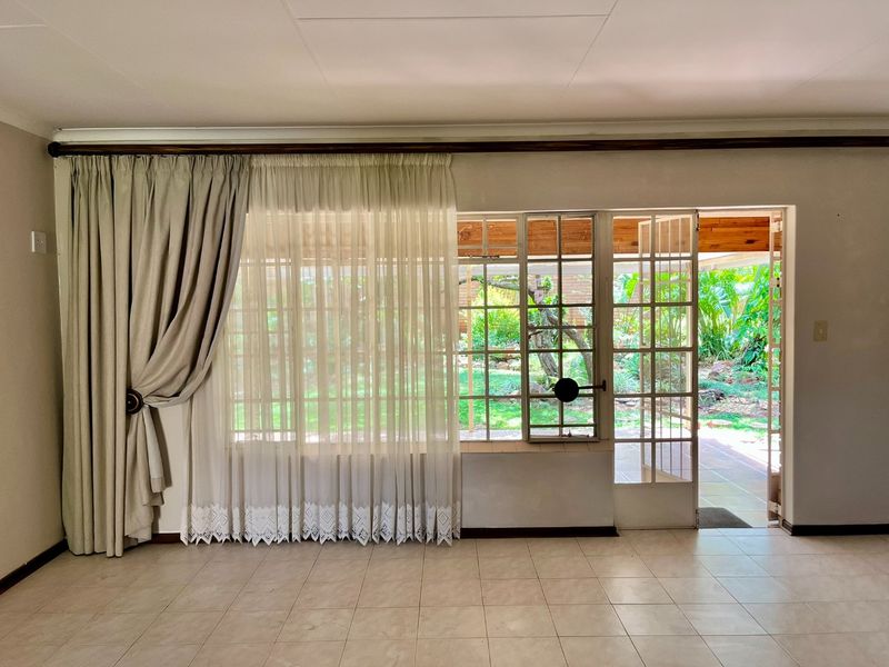 Spacious living area featuring neutral tiled flooring and large steel-framed windows and doors providing direct access to the garden.
