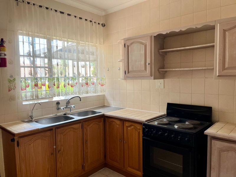 A functional kitchen featuring wooden cabinetry, a double basin sink, tiled splashbacks, and a freestanding electric stove with oven.