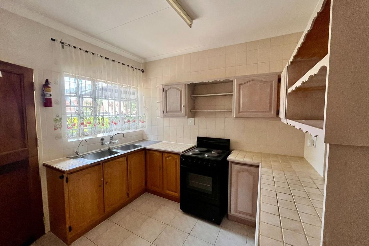 A functional kitchen featuring tiled countertops, a double sink, built-in cabinetry, and a freestanding stove, offering potential for modernization.