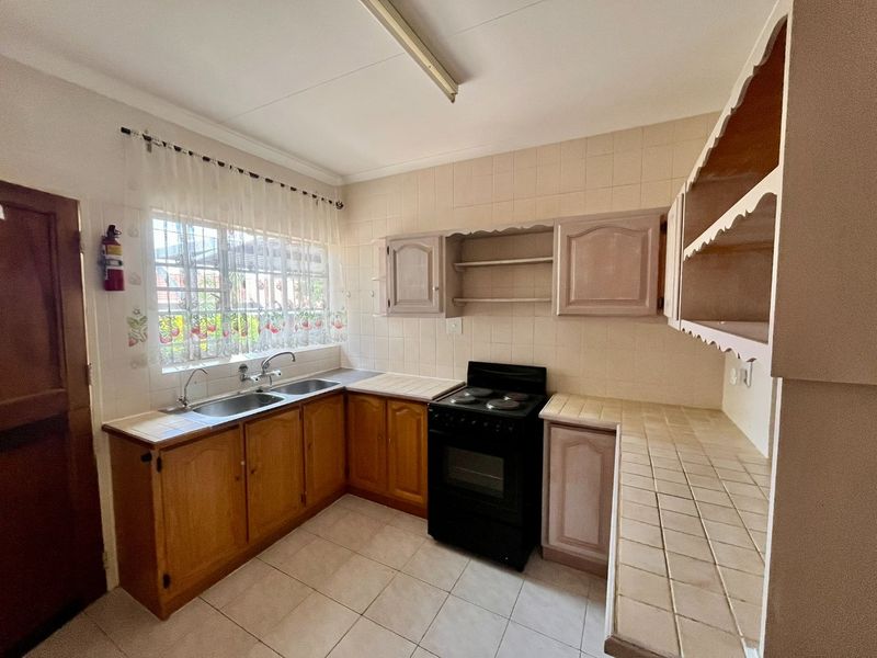 A functional kitchen featuring tiled countertops, a double sink, built-in cabinetry, and a freestanding stove, offering potential for modernization.