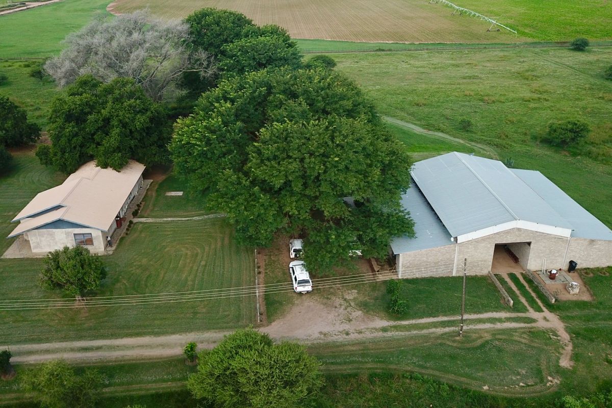 Aerial view of a farm property featuring a main dwelling and a large metal-roofed barn structure set within expansive green grounds.