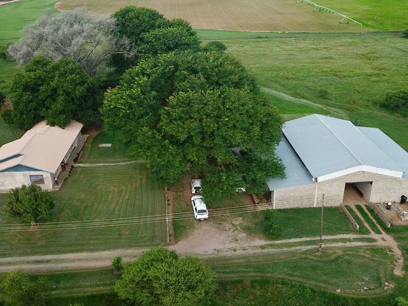 Aerial view of a farm property featuring a main dwelling and a large metal-roofed barn structure set within expansive green grounds.