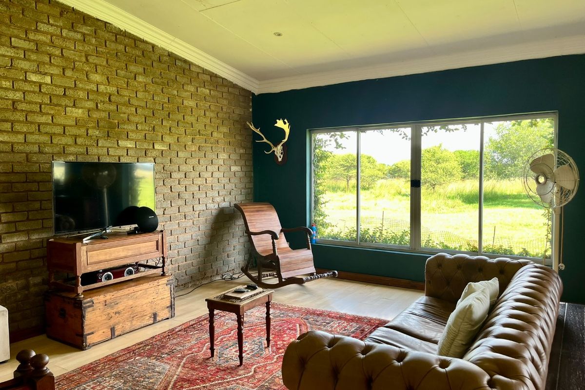 A cozy living room featuring a rustic exposed brick feature wall, large windows with scenic farm views, and modern recessed ceiling lighting.
