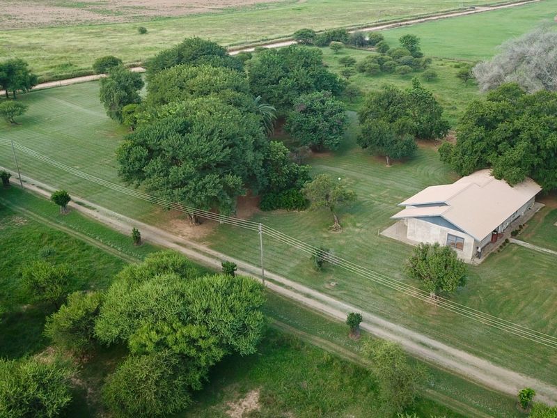 Aerial view of a farm property featuring a single-story dwelling surrounded by expansive green lawns, mature trees, and a gravel access road.