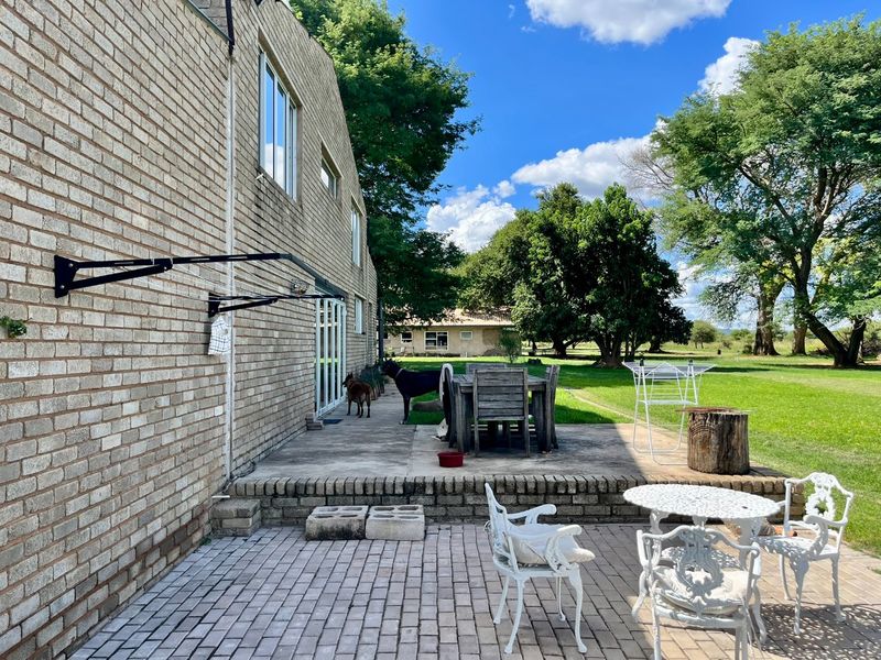 A spacious rear patio area featuring brick paving and a raised concrete terrace, overlooking a large, well-maintained garden on the farm property.