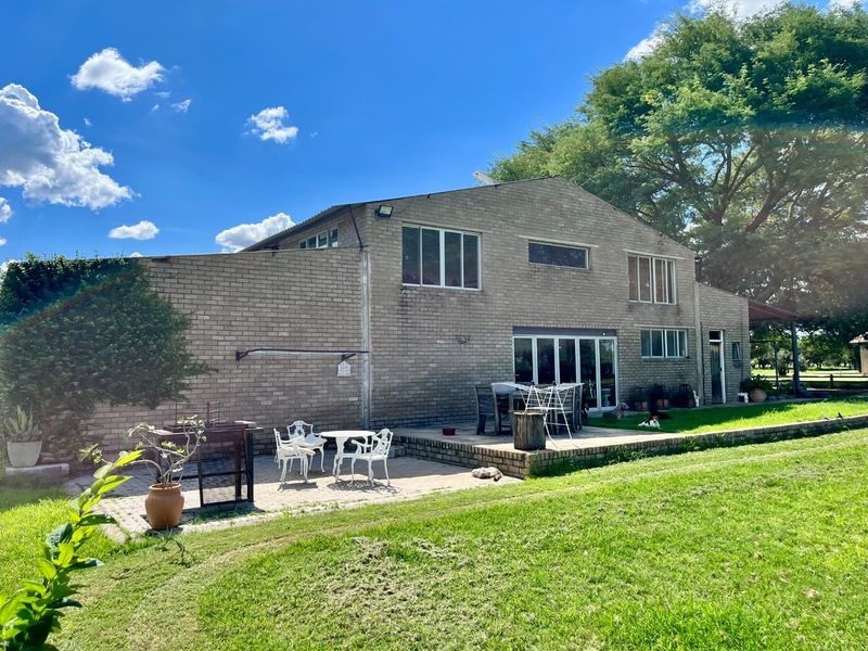 Rear view of a two-story brick farmhouse featuring a paved patio area, large windows, and expansive surrounding lawn.