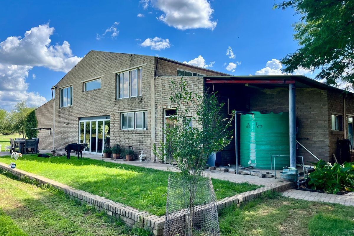 Rear view of a two-story brick farmhouse featuring a covered patio area, large water storage tank, and surrounding lawn.
