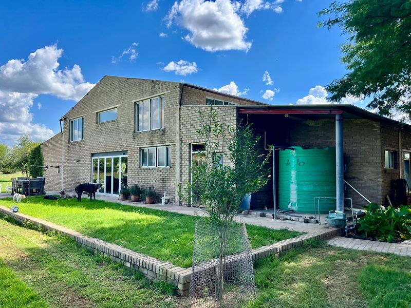Rear view of a two-story brick farmhouse featuring a covered patio area, large water storage tank, and surrounding lawn.