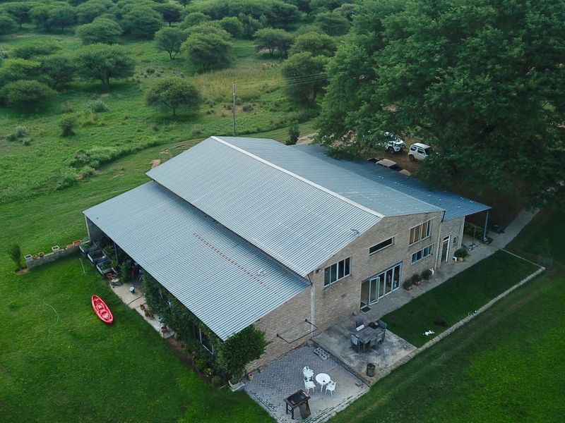 Aerial view of a large farm property featuring a spacious building with a corrugated metal roof, brick facade, and surrounding landscaped grounds.