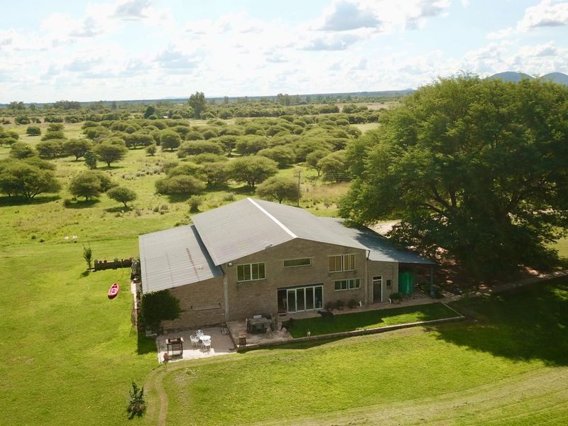 Aerial view of a large farm property featuring a spacious brick dwelling with a metal roof, set within expansive green fields and mature trees.