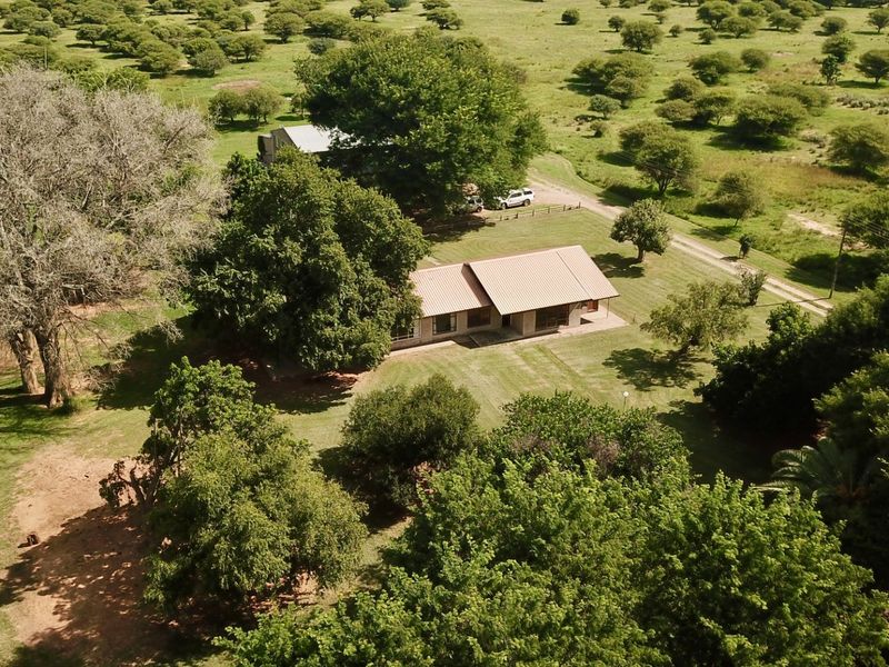 Aerial view of a farm property featuring a main dwelling with a metal roof, surrounded by expansive green lawns and mature trees.
