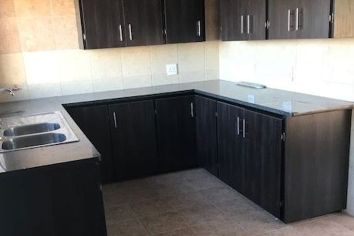 A functional kitchen featuring dark wood-finish cabinetry, granite countertops, a double-basin stainless steel sink, and tiled wall splashbacks.
