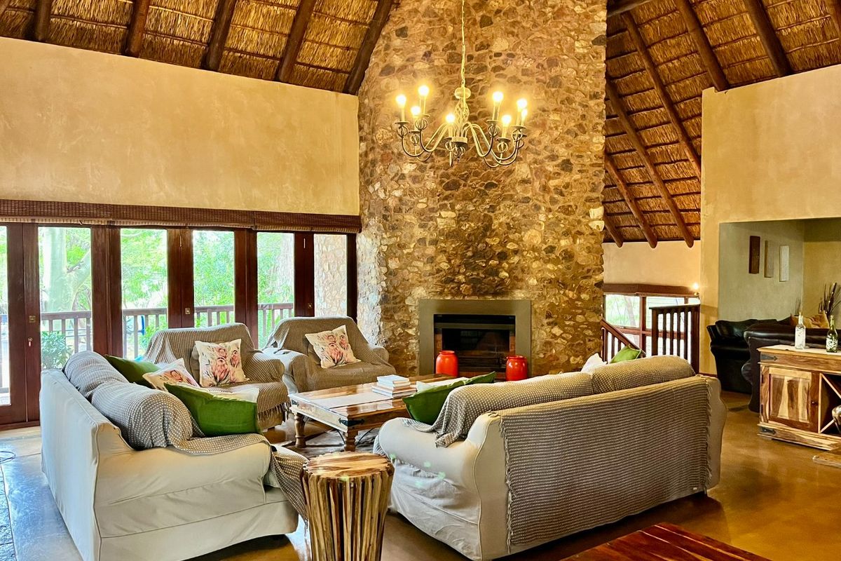 Spacious living room featuring a high vaulted thatched ceiling, a prominent floor-to-ceiling stone fireplace, and large windows overlooking the surrounding greenery.