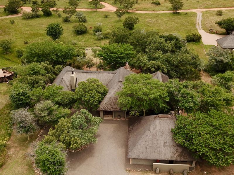 Aerial view of a thatched-roof property set within a spacious, natural bushveld landscape, featuring a driveway and surrounding greenery.