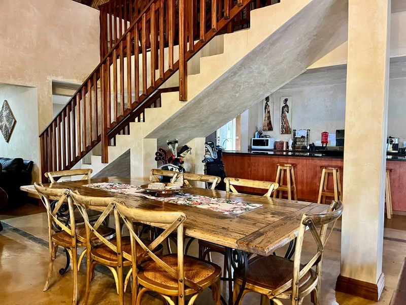 Open plan dining area featuring a prominent wooden staircase, integrated kitchen counter with bar seating, and rustic tiled flooring.