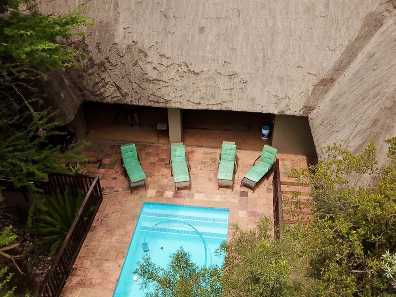 Aerial view of a private pool area featuring a tiled patio and a large thatched roof structure, surrounded by mature trees.