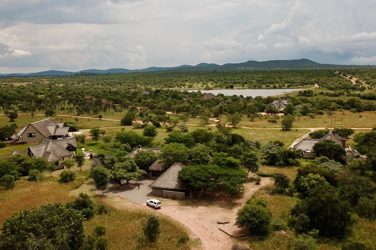 Aerial view of a sprawling bushveld estate featuring multiple thatched-roof structures set within a vast, natural landscape with a distant dam.