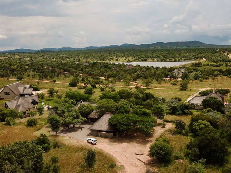 Aerial view of a sprawling bushveld estate featuring multiple thatched-roof structures set within a vast, natural landscape with a distant dam.