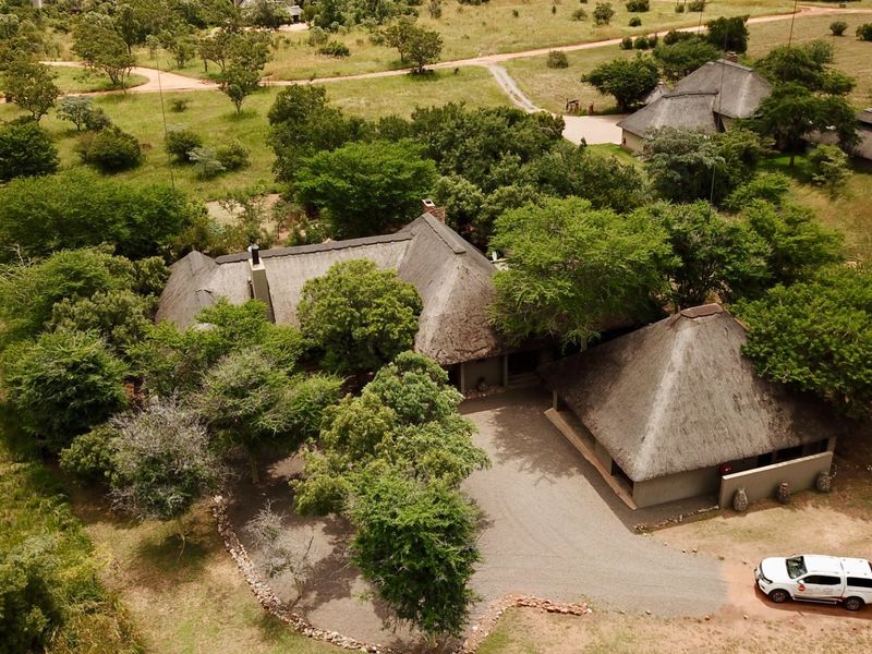 Aerial view of a bushveld property featuring multiple thatched-roof structures, a gravel driveway, and extensive natural landscaping in a serene estate setting.