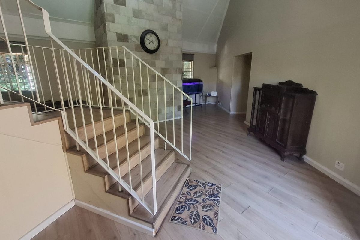 Spacious living area featuring a prominent stone fireplace, vaulted ceilings, and a staircase with a metal balustrade, finished with modern laminate flooring.