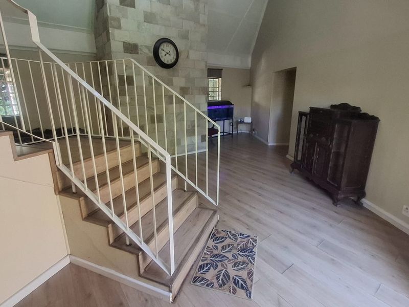 Spacious living area featuring a prominent stone fireplace, vaulted ceilings, and a staircase with a metal balustrade, finished with modern laminate flooring.