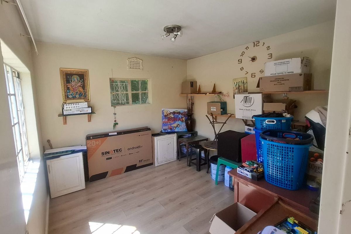 A bedroom featuring laminate flooring and steel window frames, currently used as a storage space with built-in cupboard units.