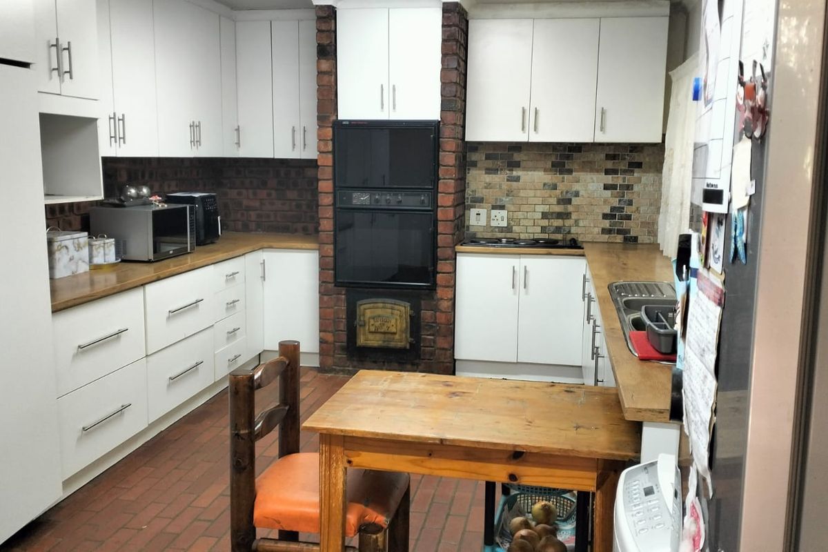 A functional kitchen featuring white cabinetry, brick feature wall with built-in oven, tiled backsplash, and brick flooring.