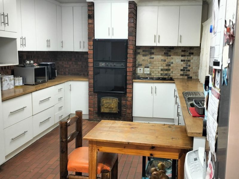 A functional kitchen featuring white cabinetry, brick feature wall with built-in oven, tiled backsplash, and brick flooring.