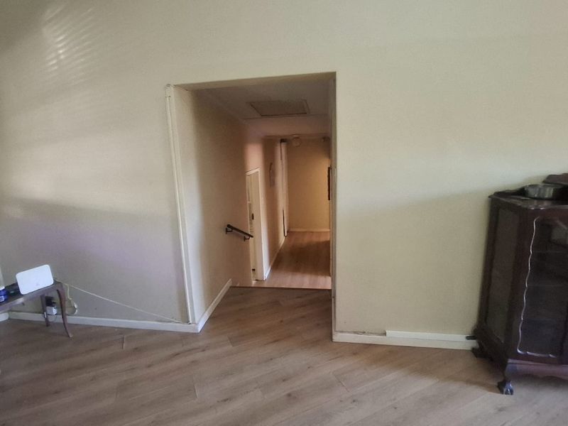 A view of a hallway transition area featuring laminate flooring and a handrail, showing signs of wear and incomplete trim work.