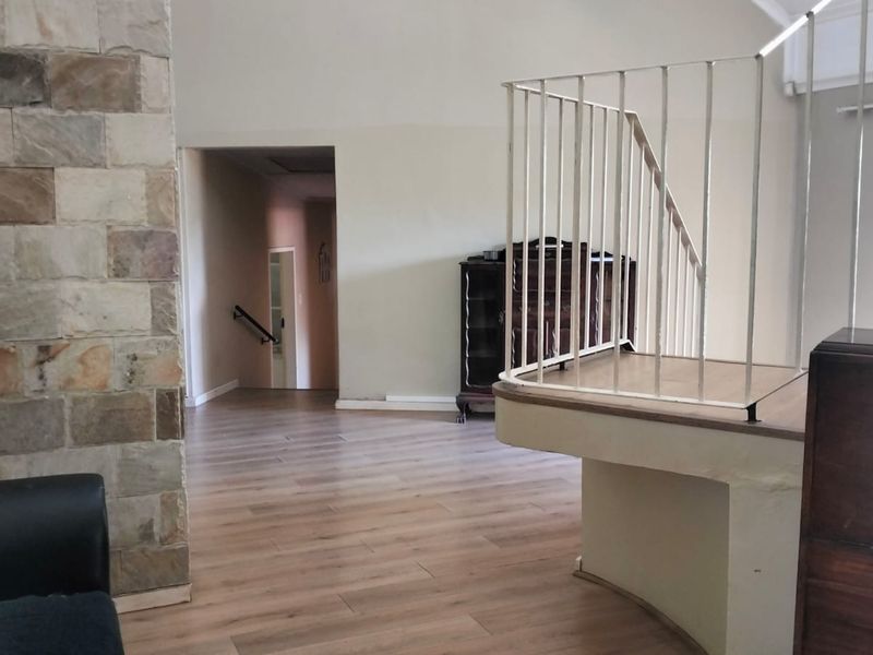 Spacious living area featuring a stone accent wall, vaulted ceilings, and a staircase with a metal balustrade, finished with modern laminate flooring.