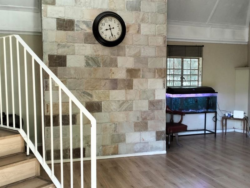 Living area featuring a prominent stone feature wall, laminate flooring, and a staircase with a white metal railing under a vaulted ceiling.