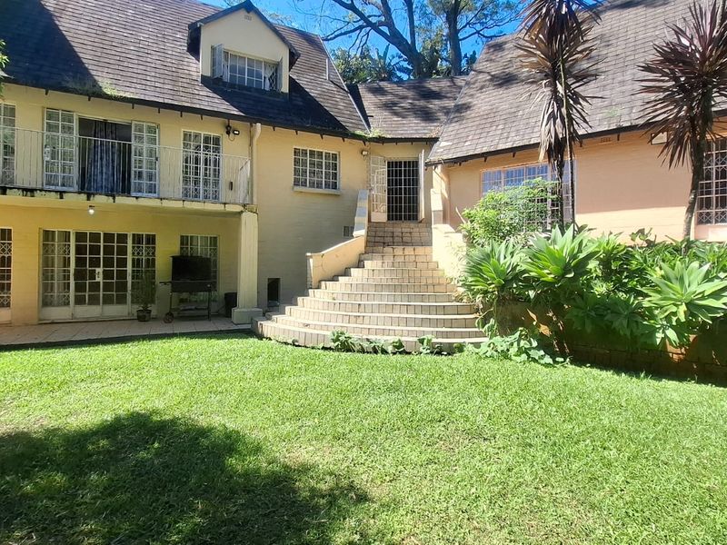 Rear view of a multi-story house featuring a lawn, a tiled patio area, and a central concrete staircase leading to the upper level.