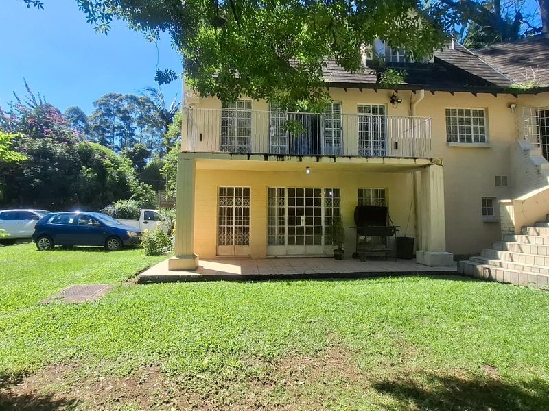 Rear view of a two-story house featuring a ground-level tiled patio, an upper-level balcony with metal railings, and an external staircase leading to the garden.
