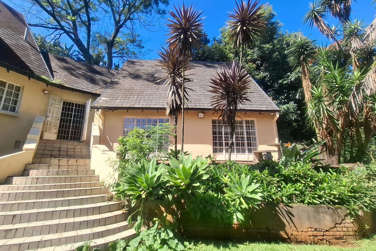 Rear view of the property featuring a tiled staircase, shingle roofing, and a brick retaining wall set within a mature garden.