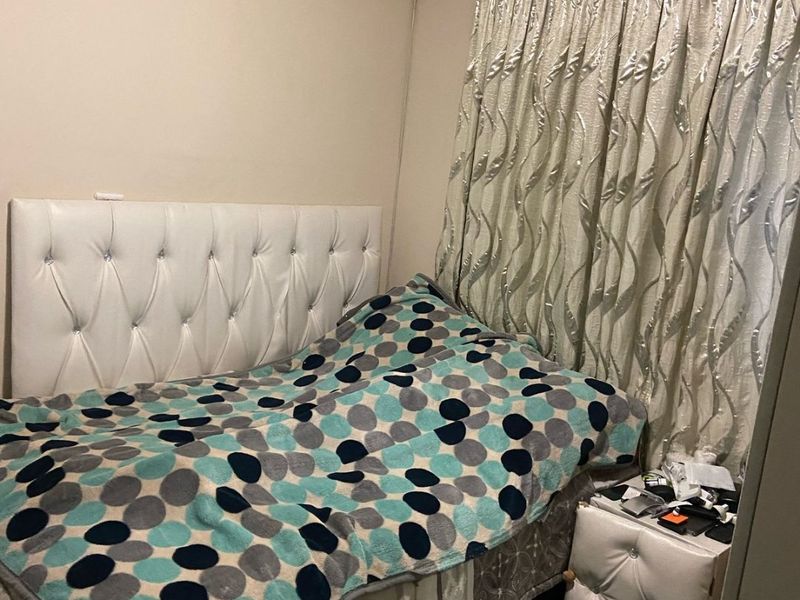 A compact bedroom featuring a wall-mounted air conditioning unit and window curtain rails.