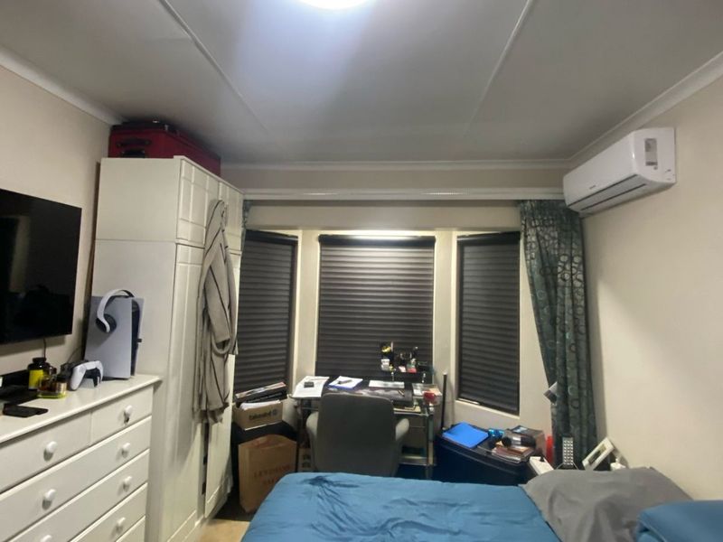 A functional bedroom featuring a built-in wardrobe, split-system air conditioning, and a bay window with fitted roller blinds.