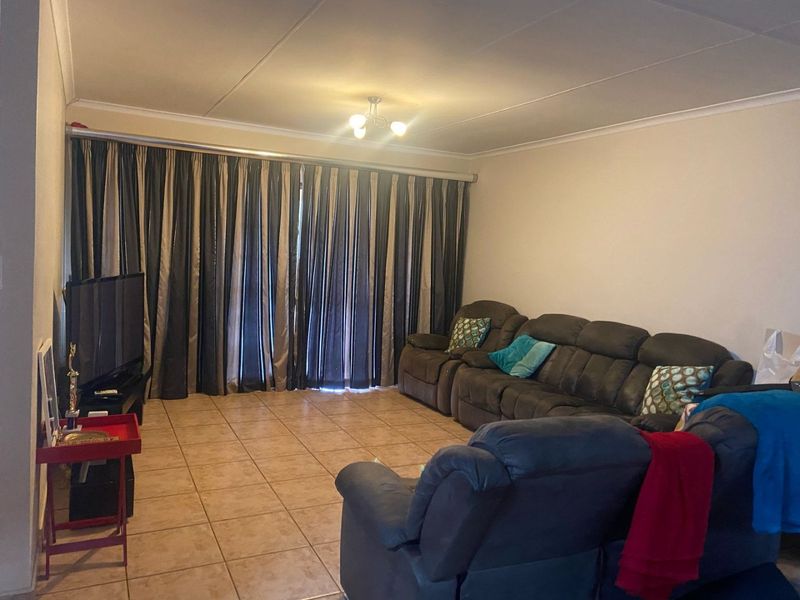 A spacious living room featuring neutral wall tones, tiled flooring, and large floor-to-ceiling curtains providing access to the outdoor area.