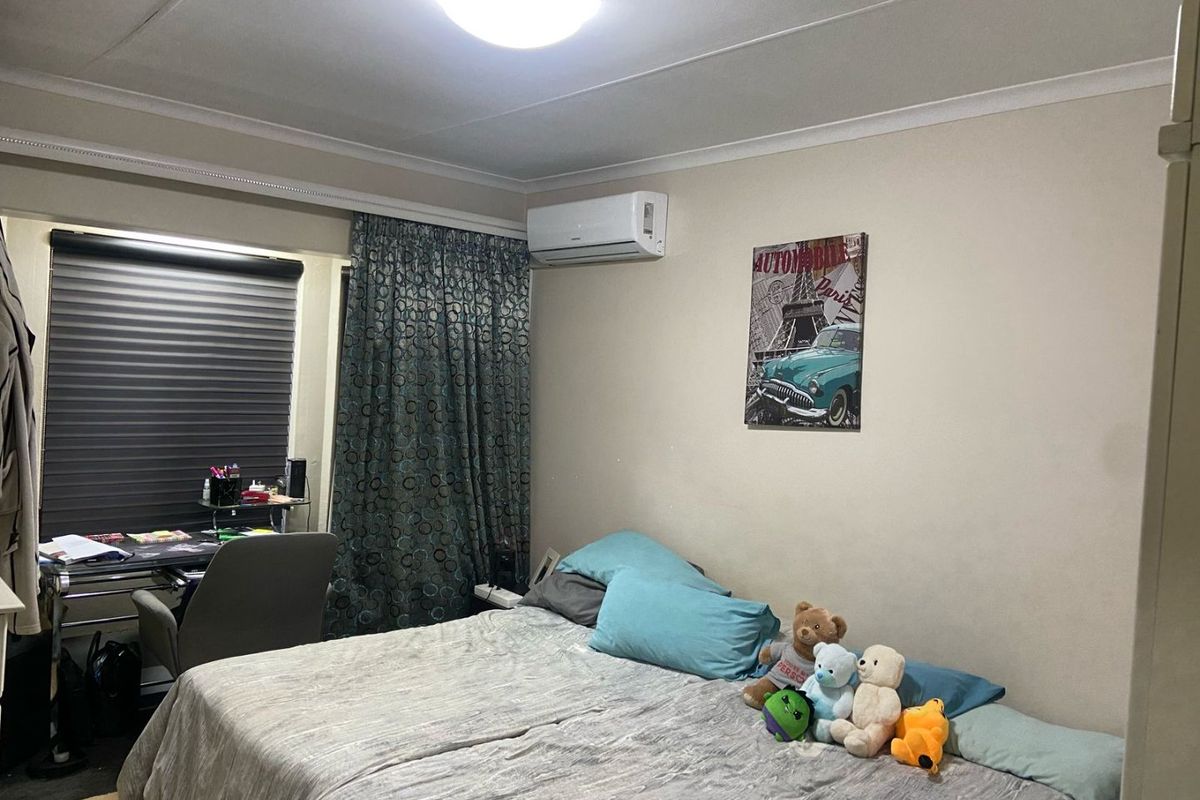 A functional bedroom featuring a wall-mounted air conditioning unit, window blinds, and curtain tracks, providing a comfortable living space.