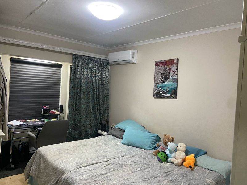 A functional bedroom featuring a wall-mounted air conditioning unit, window blinds, and curtain tracks, providing a comfortable living space.