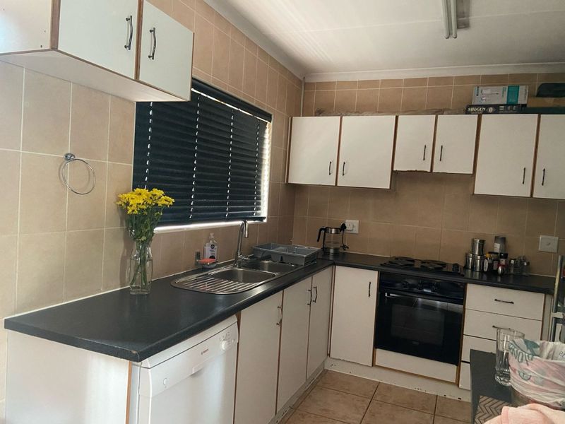 A functional kitchen featuring white cabinetry, dark laminate countertops, a built-in oven and hob, and neutral tiled backsplash and flooring.
