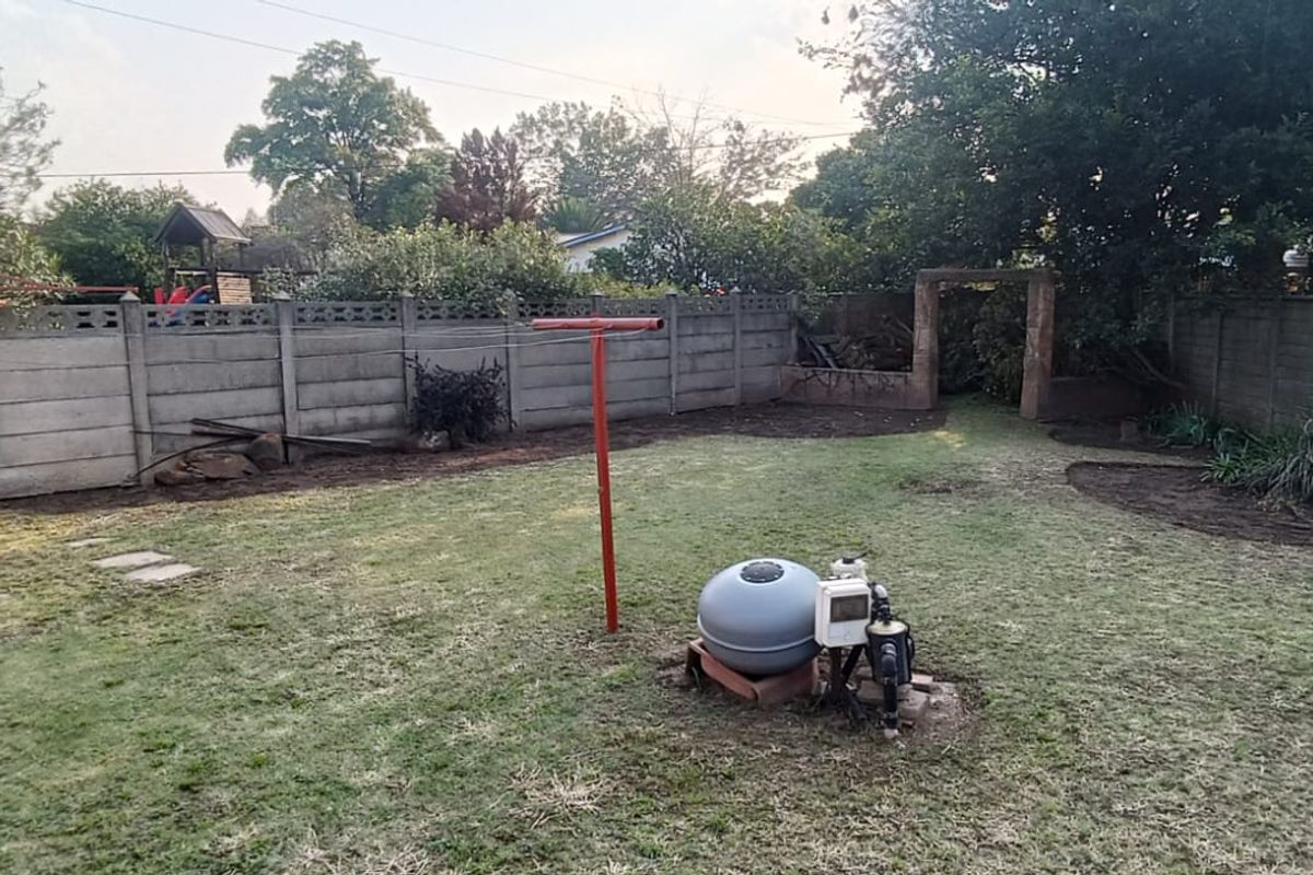 A spacious rear garden featuring a concrete boundary wall, lawn area, and exposed pool filtration system.