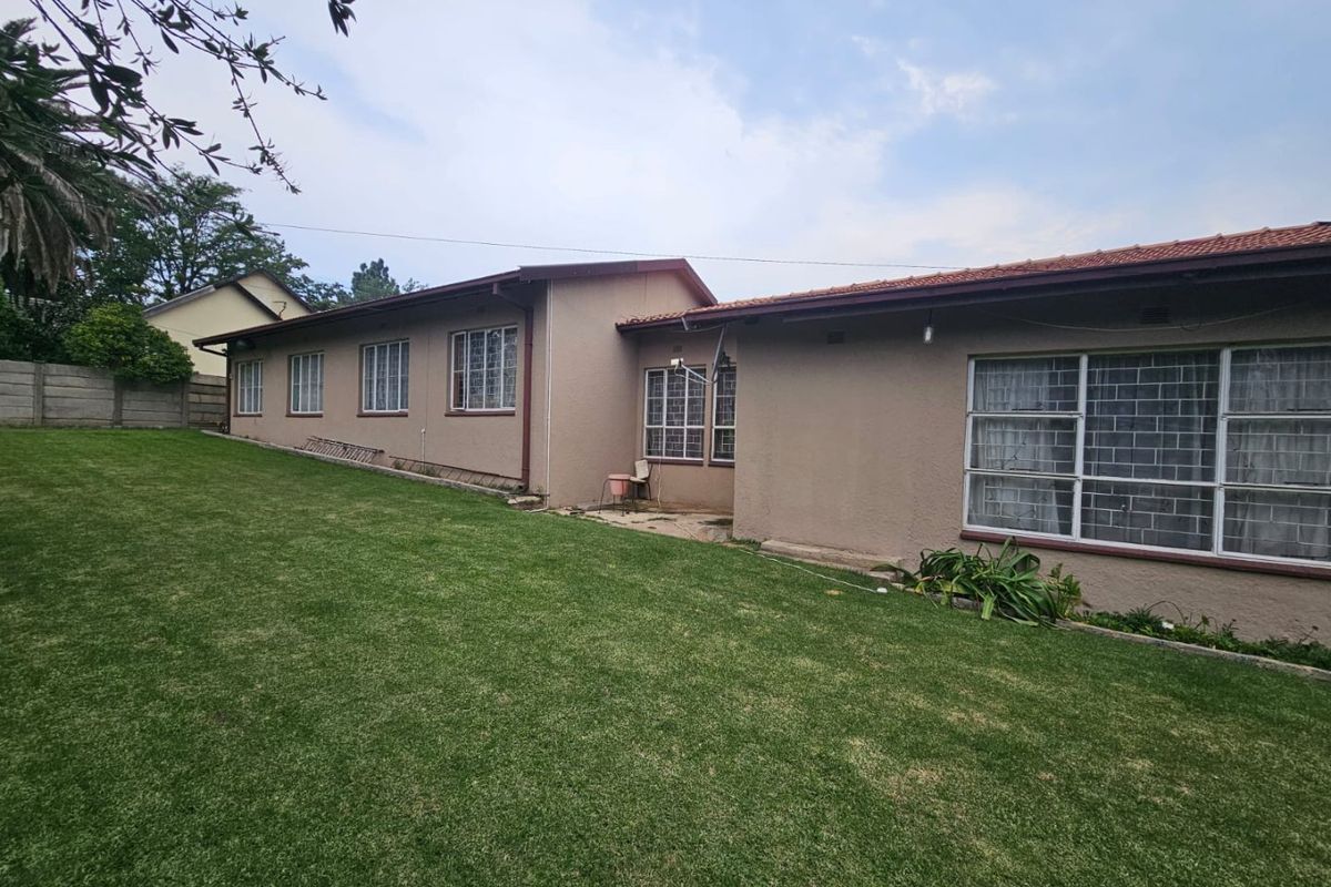 A view of the rear exterior of the house, featuring a large lawn area and multiple windows with security bars.